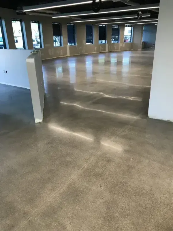 Empty modern office interior with polished concrete floors and white walls, lit by overhead lights and windows