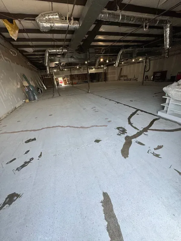Empty industrial warehouse with cracked white concrete floor and exposed ceiling pipes and ducts