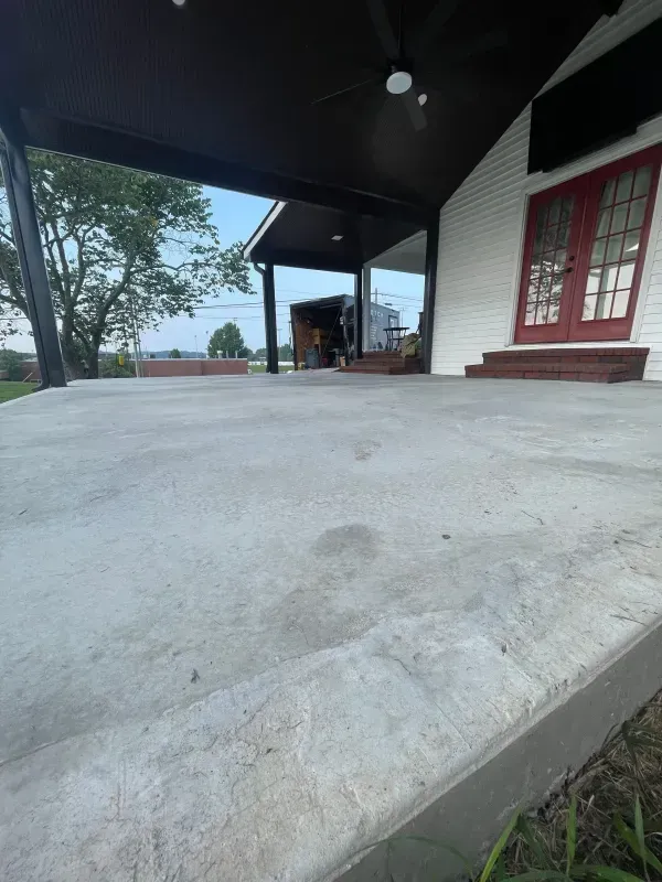 Concrete ramp beside a white building with red doors and a covered porch overlooking trees and water