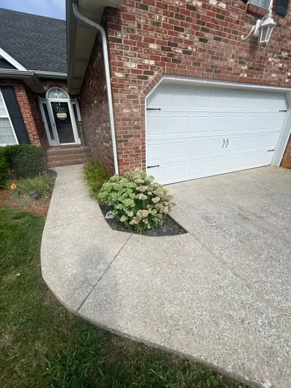 Brick house driveway with white garage door, curved concrete path, and small flower bed by the entrance