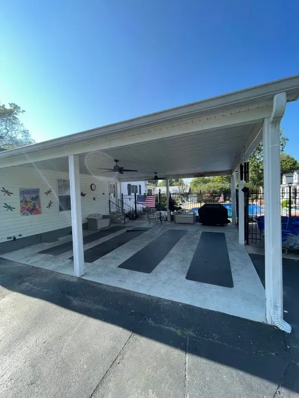Covered carport with concrete ramps, striped mats, and a parked car on a sunny day