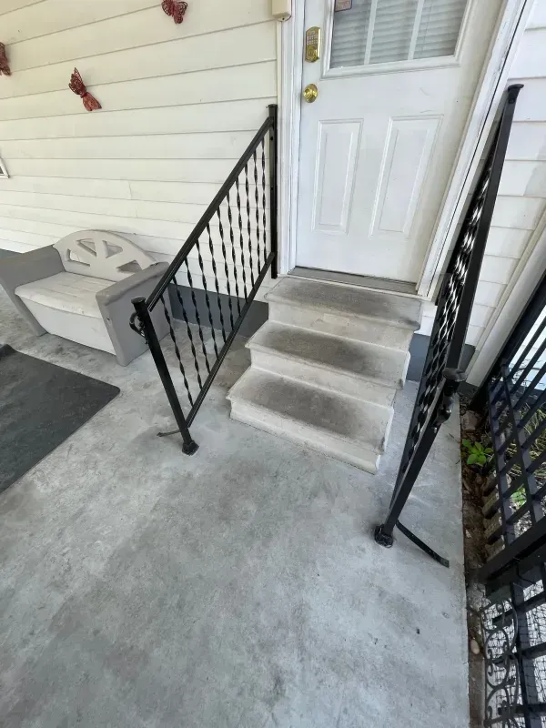 Front porch steps with black railings leading to a white front door and a concrete landing
