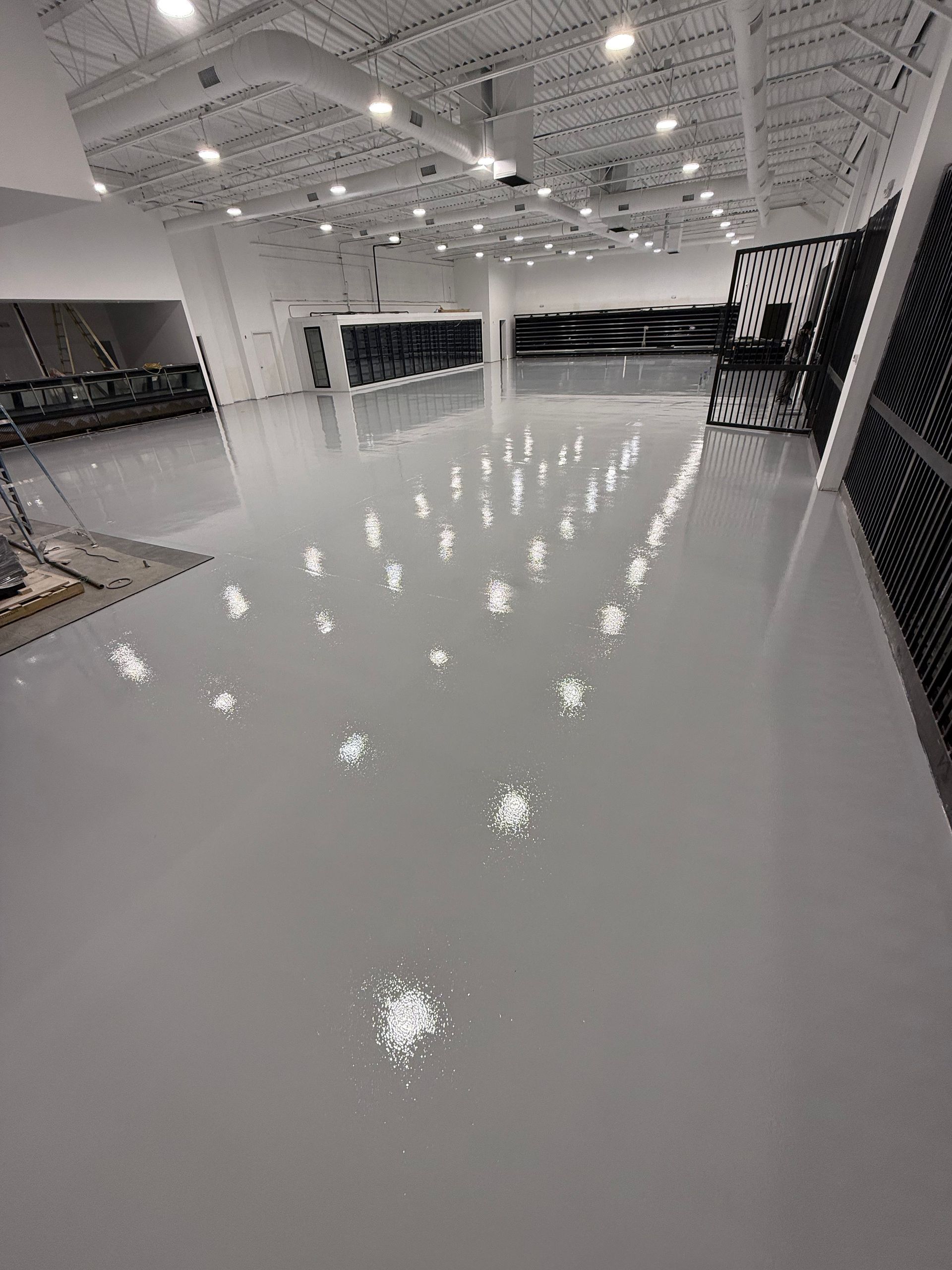 Glossy indoor sports court with white floor, overhead lights, and side netting under construction