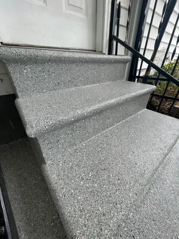 Gray speckled front steps leading to a white door with a black railing