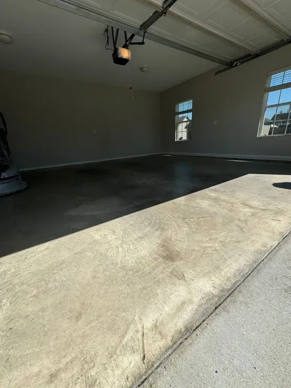 Empty garage with a concrete floor, white walls, and sunlight from windows and the open door.