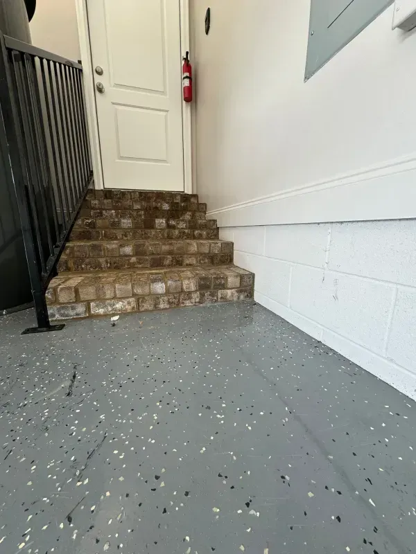 Indoor stairwell with brick steps, white door, black railing, and a red fire extinguisher on the wall.