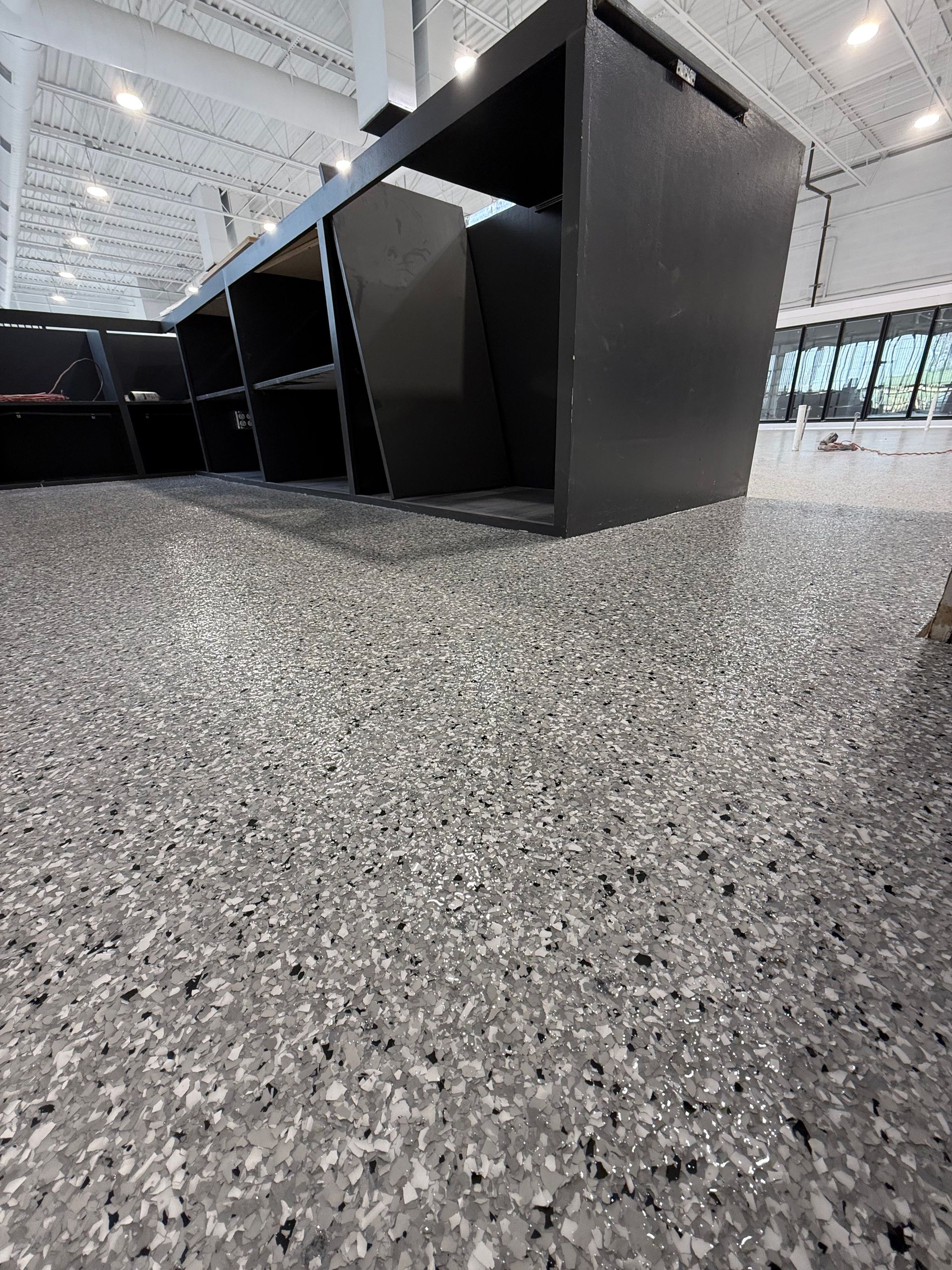 Black cubicle desks on a speckled carpet in a bright, modern office space.