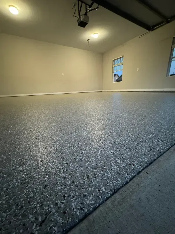 Empty garage with speckled epoxy floor, cream walls, and overhead lights