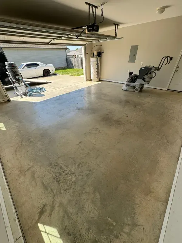 Empty garage with a concrete floor, open door, a car in the driveway, and yard tools along the walls