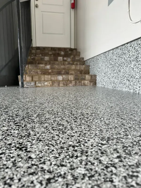 Speckled floor leading to a short stone stairway and white door in a narrow hallway