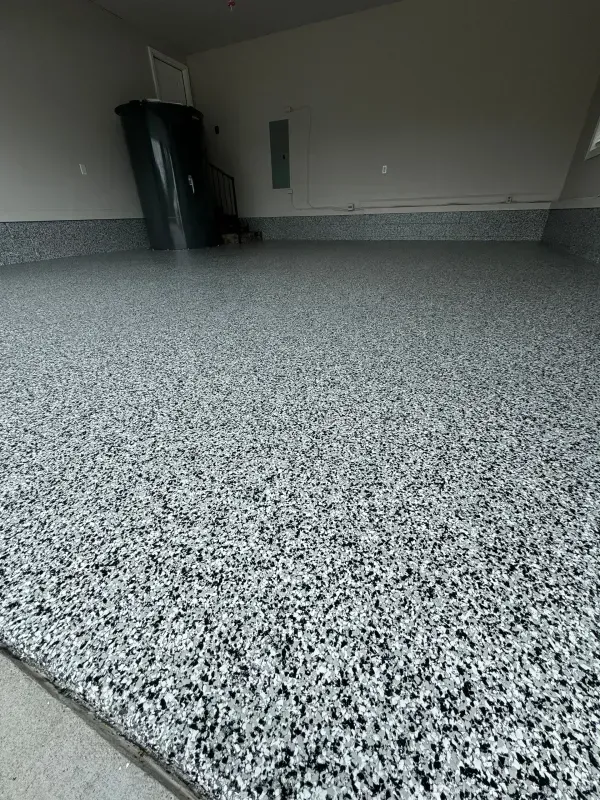 Empty indoor garage with a speckled floor and a trash bin near the wall