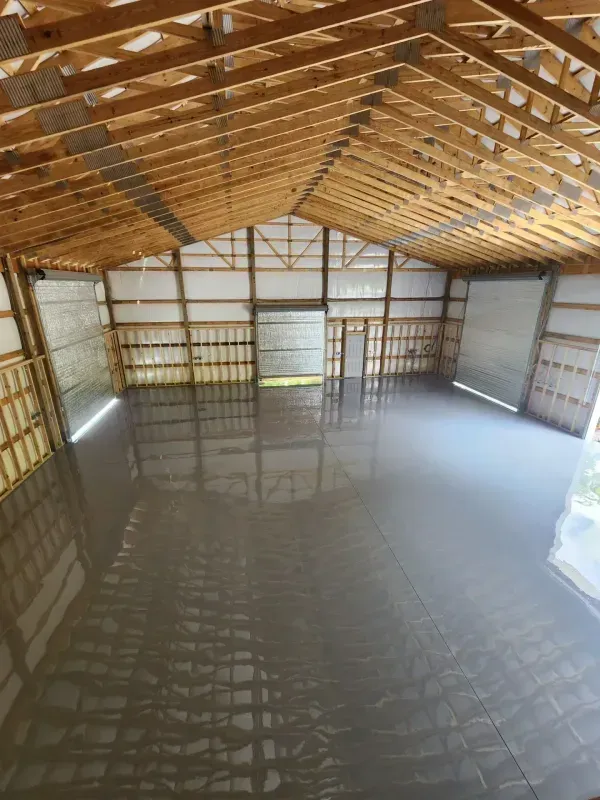 Empty warehouse interior with unfinished wood roof trusses and a glossy concrete floor
