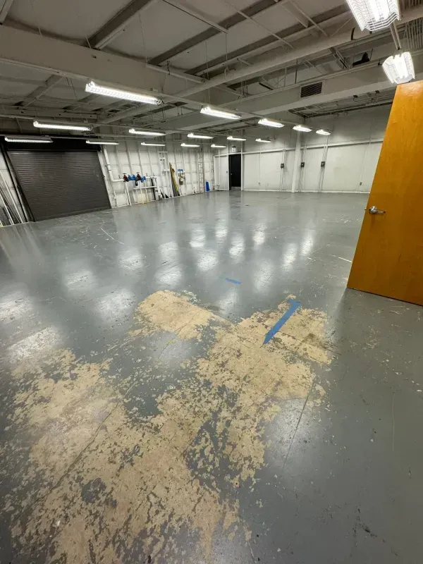 Empty industrial room with gray floor, white walls, exposed ceiling, and a wooden door on the right