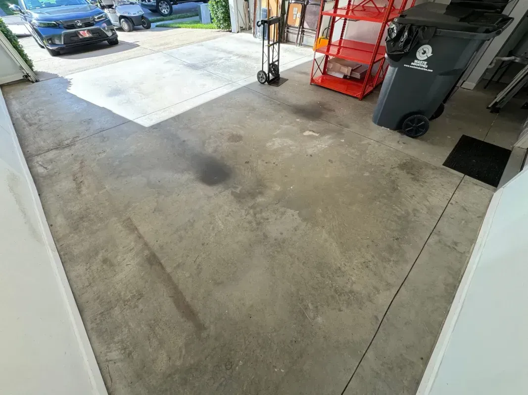 Open garage with concrete floor, red tool cart, trash bin, and a car parked outside.