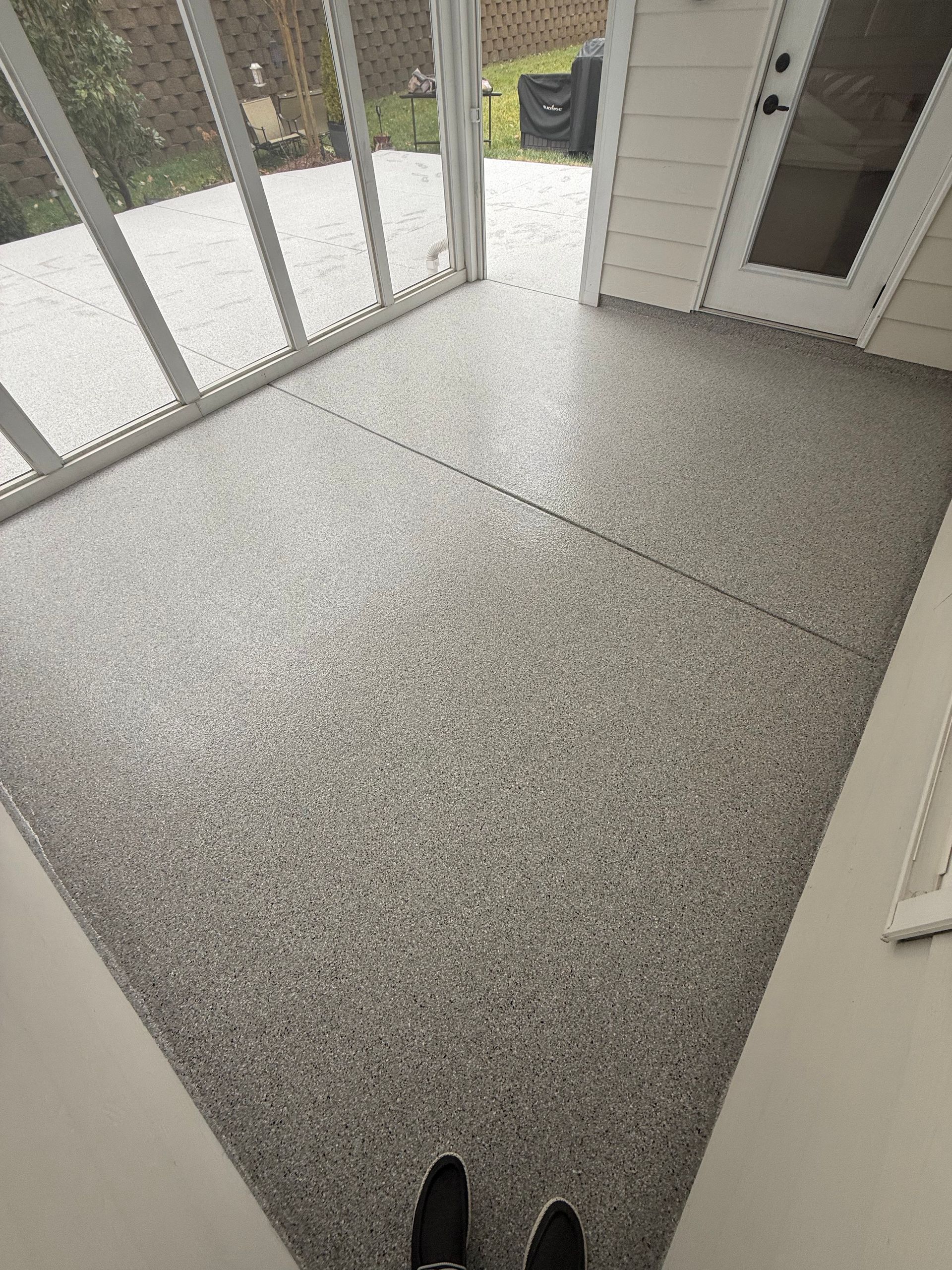 Enclosed porch with speckled gray floor, screen windows, and a black shoe visible at the bottom.