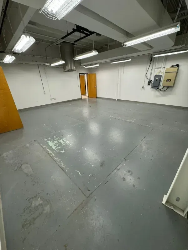 Empty industrial room with gray floor, white walls, fluorescent lights, and orange double doors