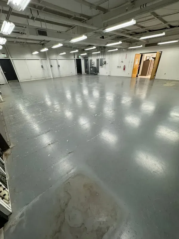 Empty gray industrial room with white ceiling lights and open wooden doors in the back.