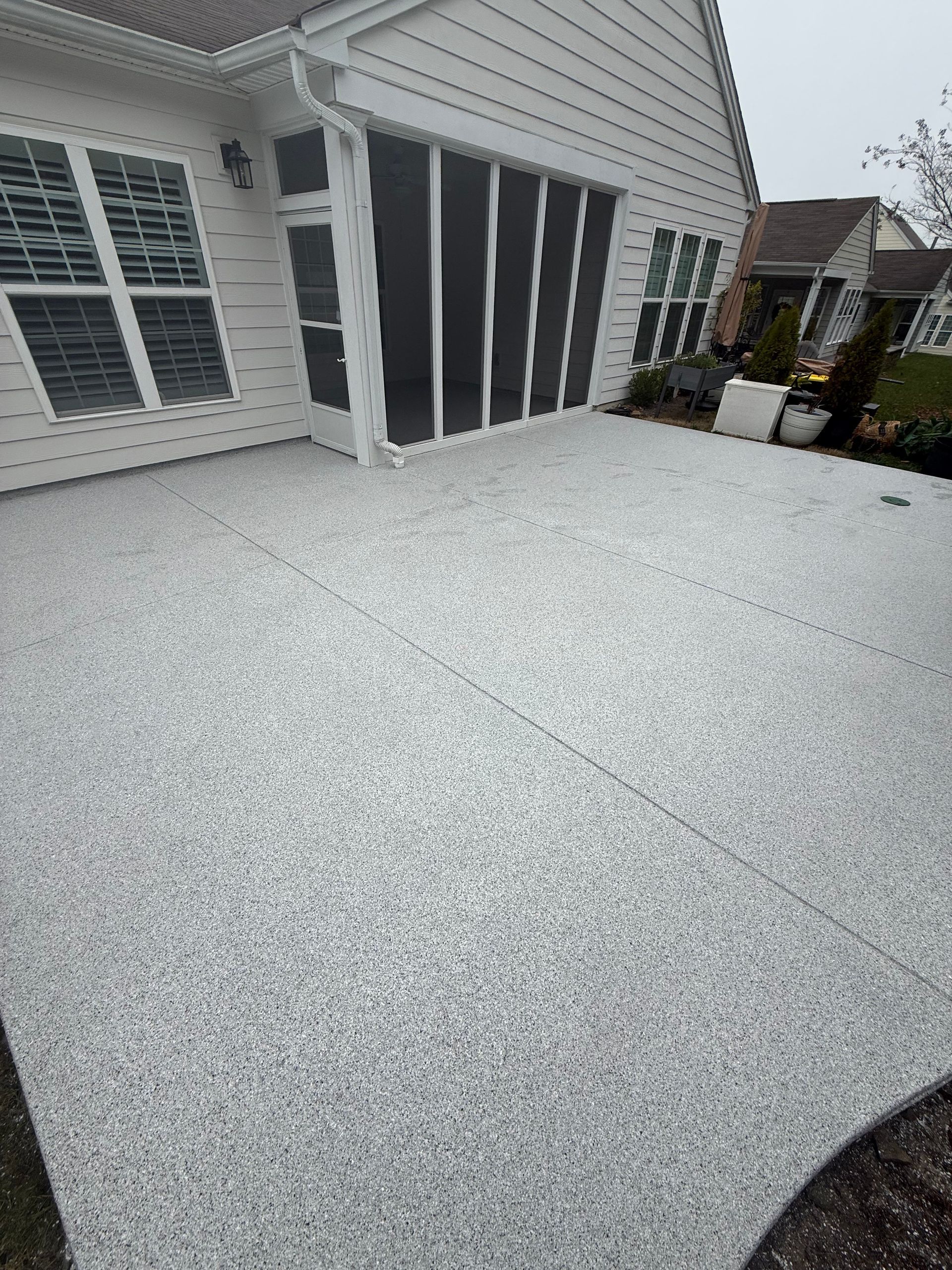 Screened patio with white speckled flooring beside a house, overlooking a backyard and hot tub.