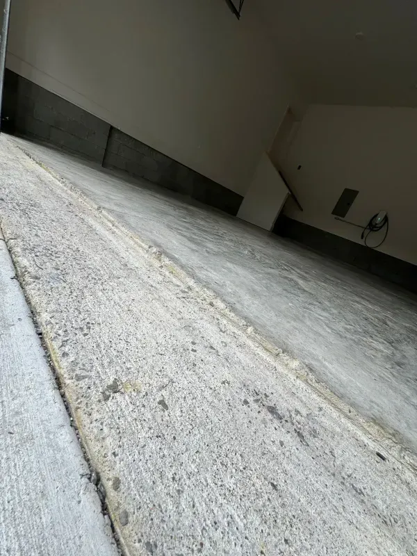 Tilted view of a concrete driveway or garage floor with a yellow center line near a wall