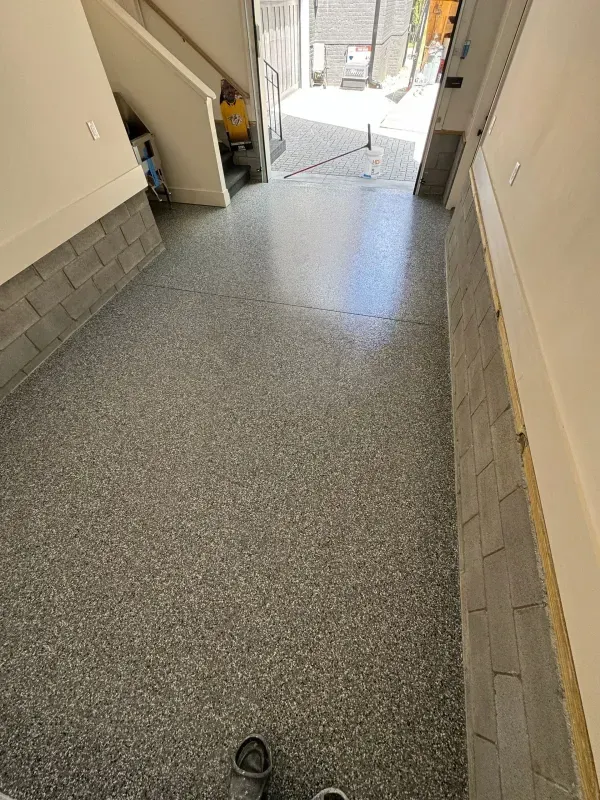 Hallway with speckled floor leading to a bright outdoor entryway, with a shoe at the bottom edge