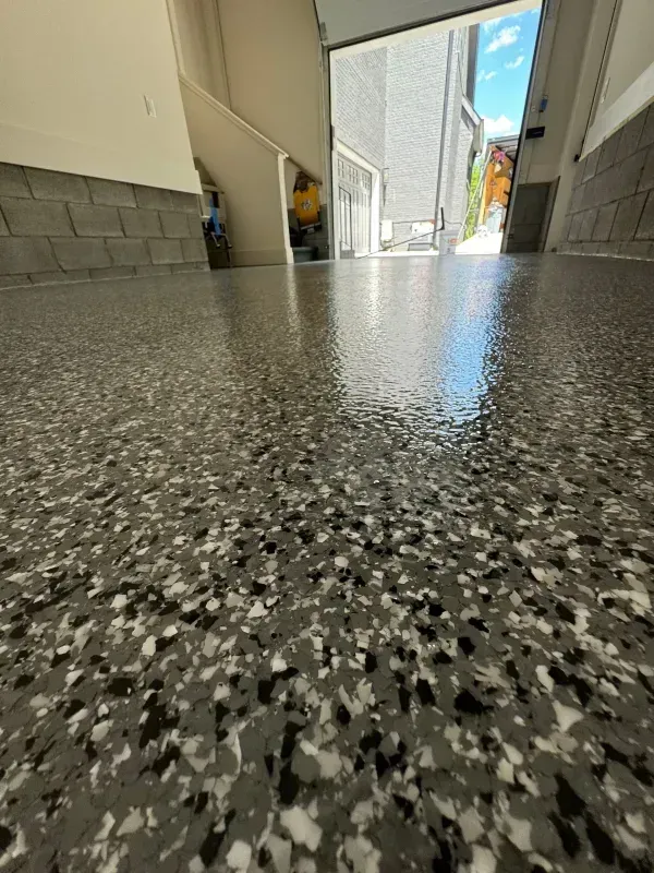 Low-angle view of a speckled hallway floor leading to a bright outdoor street.