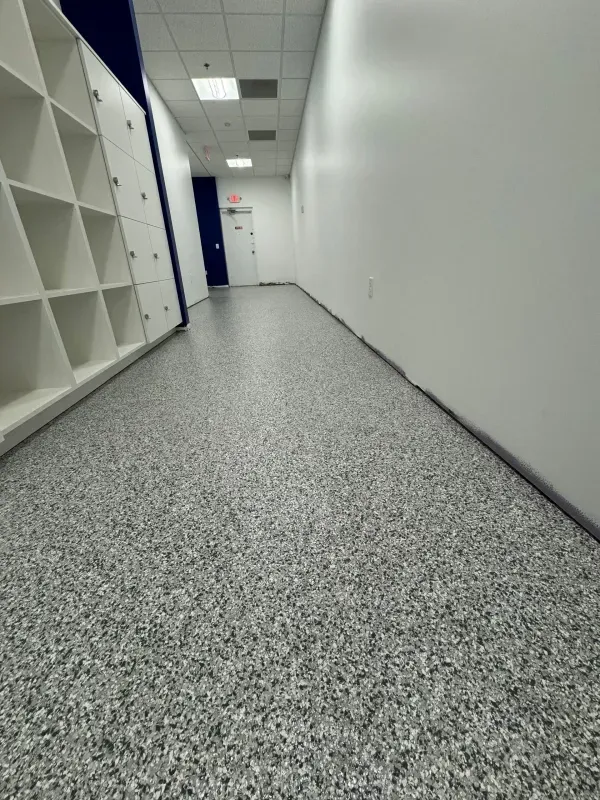 Empty office hallway with white walls, gray speckled carpet, and shelving along the left side.
