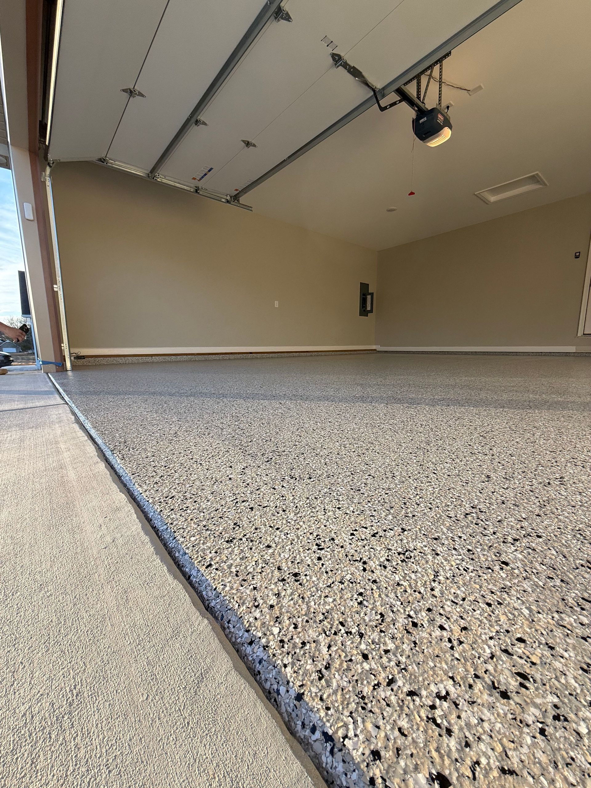 Empty garage with speckled concrete floor and partially open overhead door.