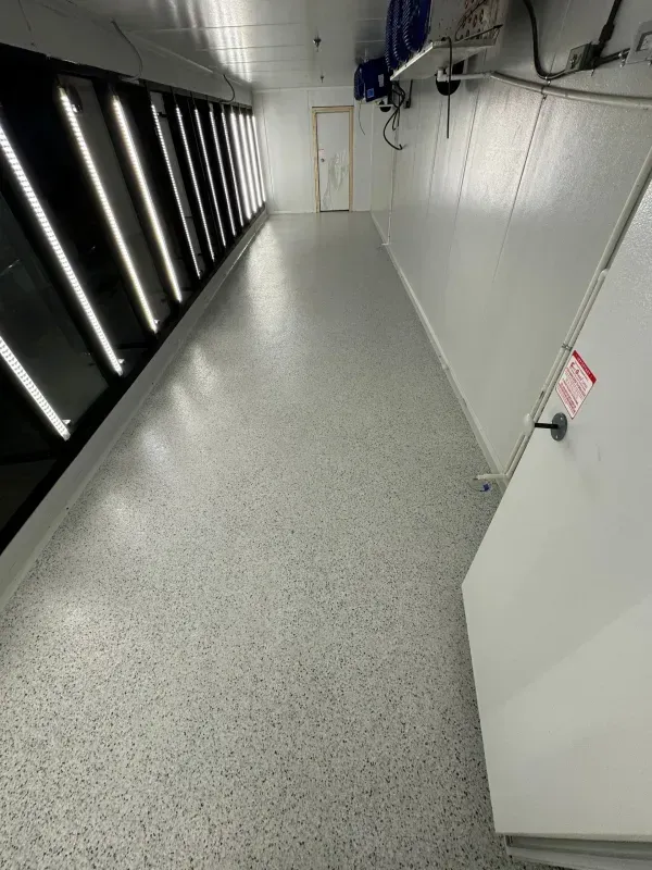 Empty server room aisle with black cabinets, gray speckled floor, and white wall panels.