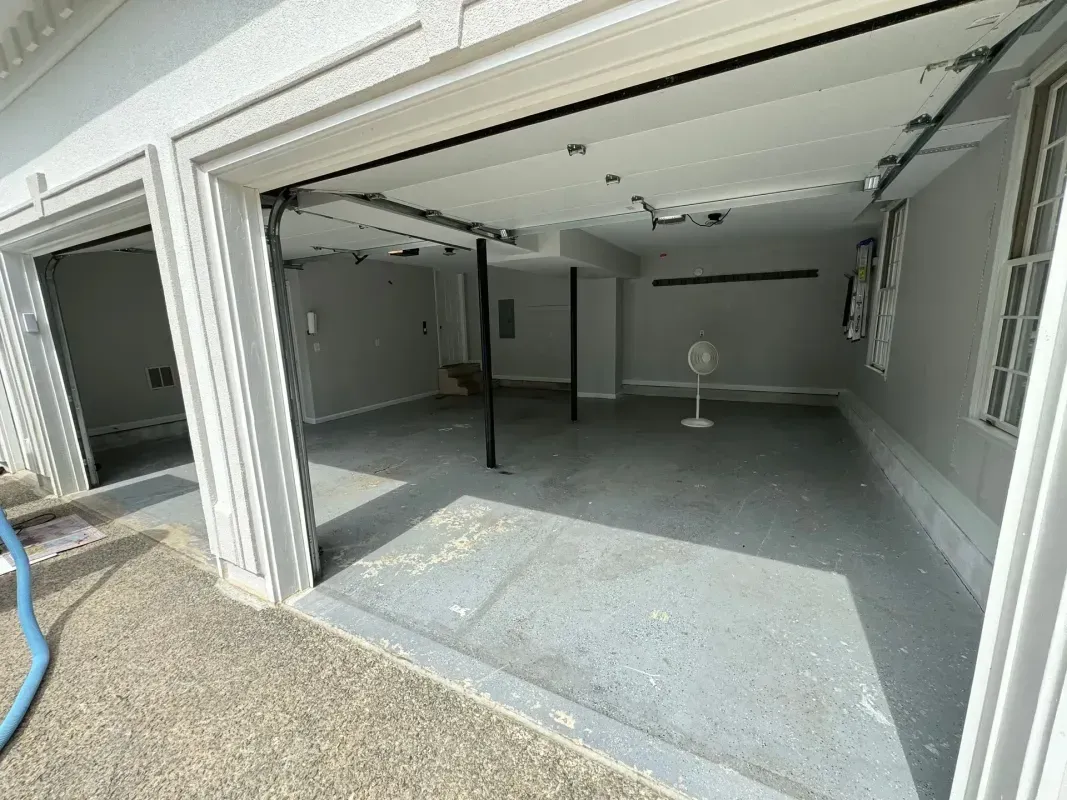 Empty garage with open double doors, gray concrete floor, and a standing fan inside.