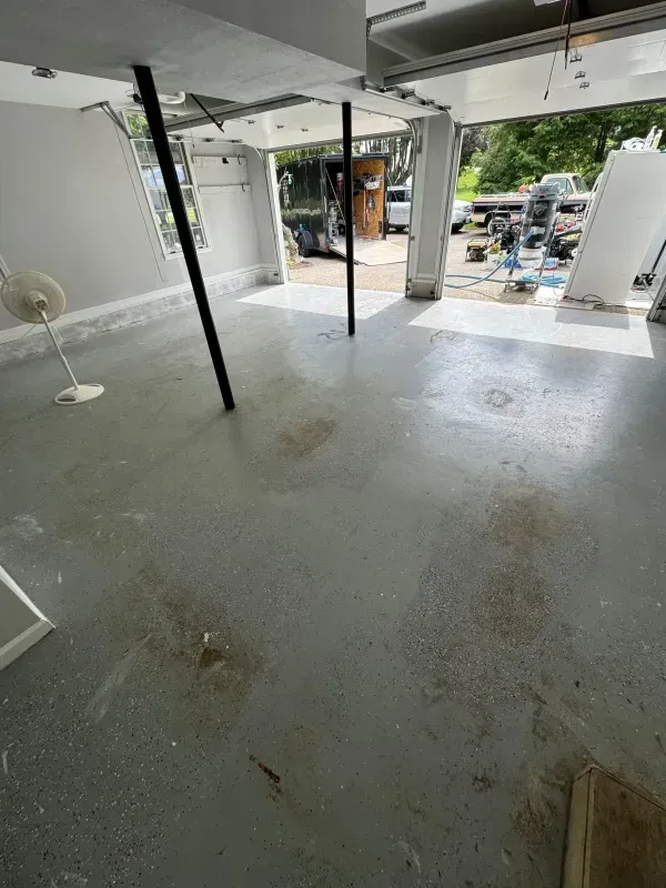 Flooded indoor garage with wet concrete floor and open view to the driveway outside