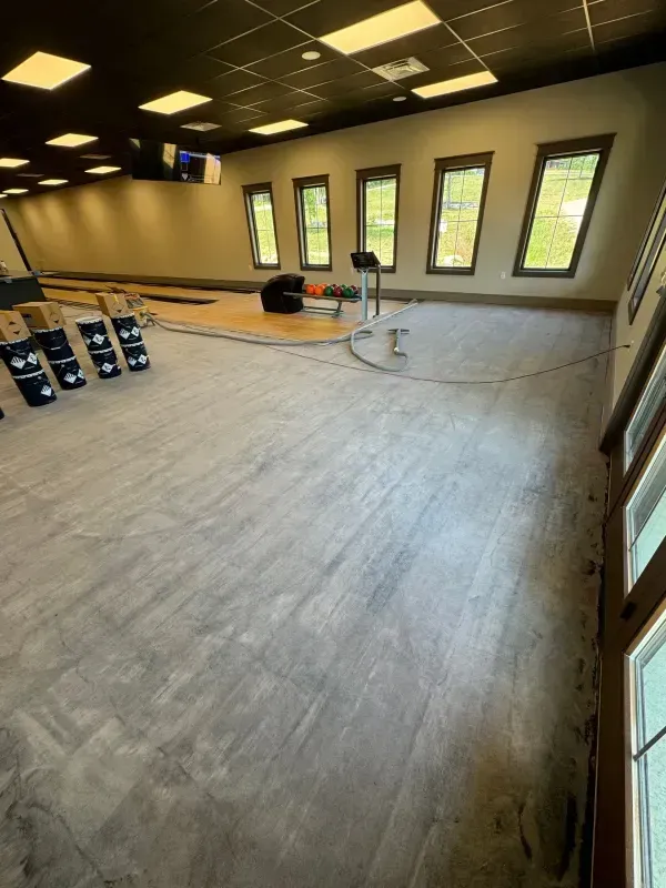 Empty studio with gray floor, black ceiling lights, wall mirrors, windows, and stacked dumbbells.