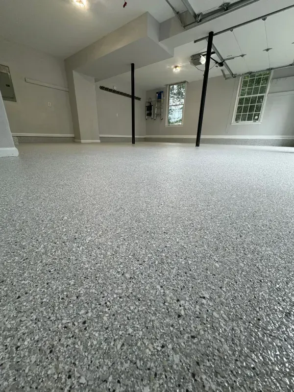 Empty garage with speckled epoxy floor, exposed ceiling, black support posts, and windows.