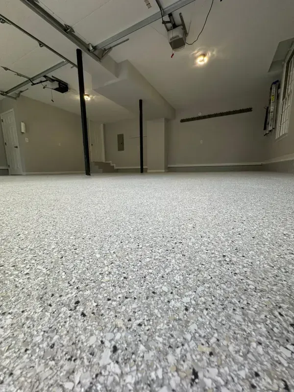 Empty garage with speckled epoxy floor, white walls, and ceiling-mounted garage door tracks