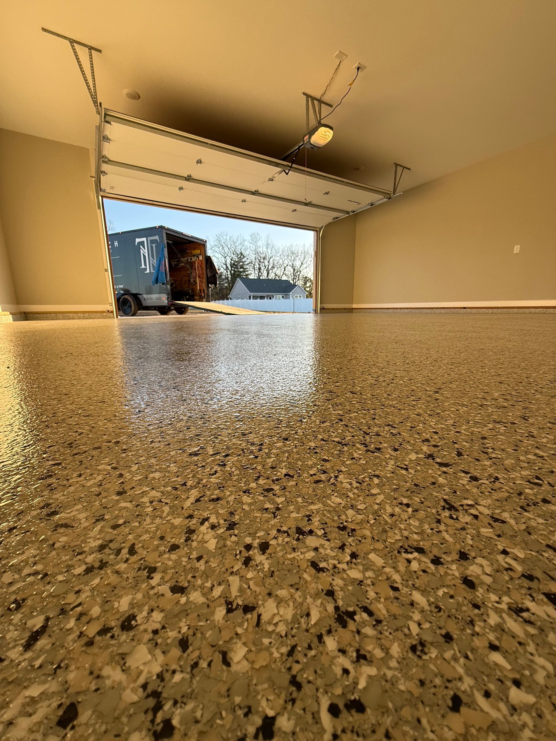 Flooded garage with water covering a speckled floor, open door showing a truck and snow outside.