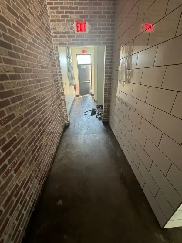 Narrow brick hallway with EXIT signs, tiled wall, and a doorway at the far end.