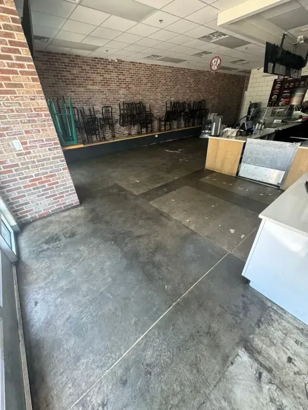 Empty brick-walled café area with dark tiled floor, stacked chairs, and counters along the side