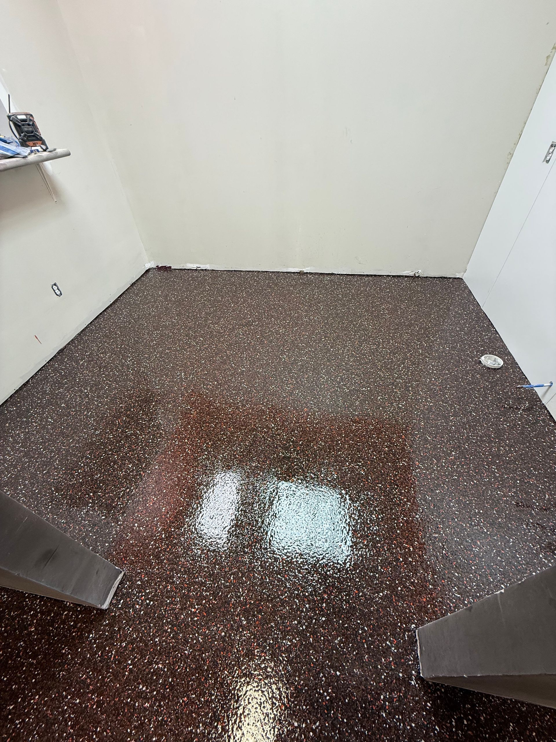 Small empty room with brown speckled floor and a bright light reflection in the center.