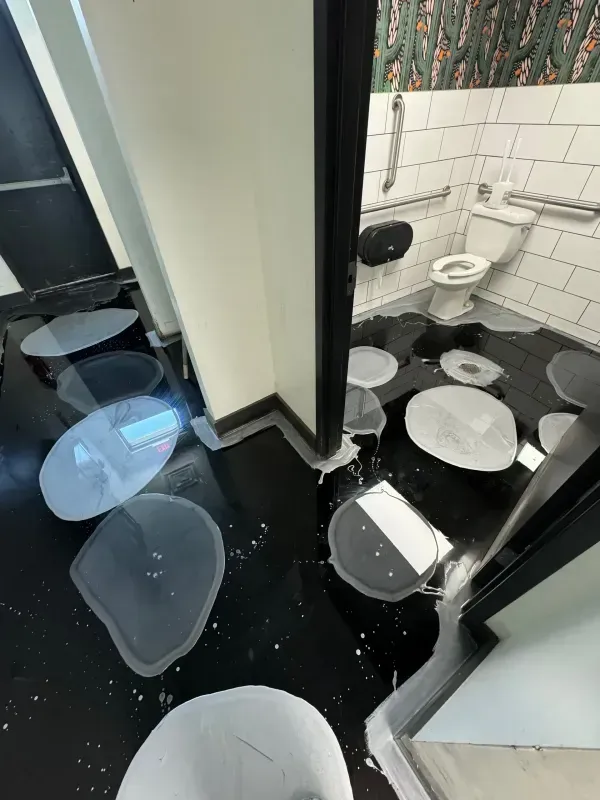 Modern bathroom with white tiled walls, black floor, and several broken glass pieces scattered on the floor.