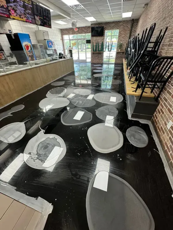 Empty restaurant floor with white circles taped for social distancing and stacked chairs on tables