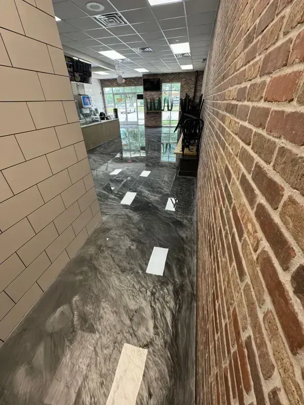 Damaged office hallway with cracked floor, exposed base, brick wall, and debris near glass entrance