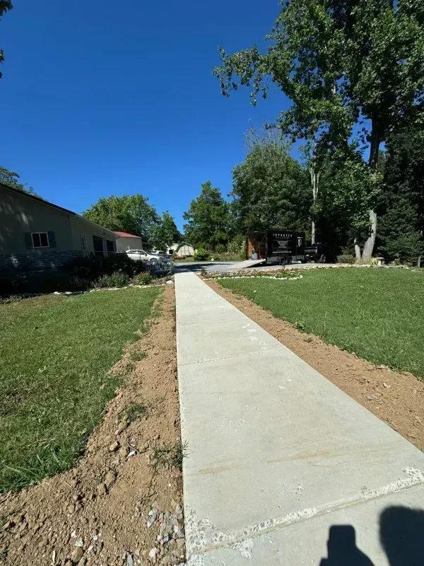 New concrete sidewalk through a grassy yard under a clear blue sky
