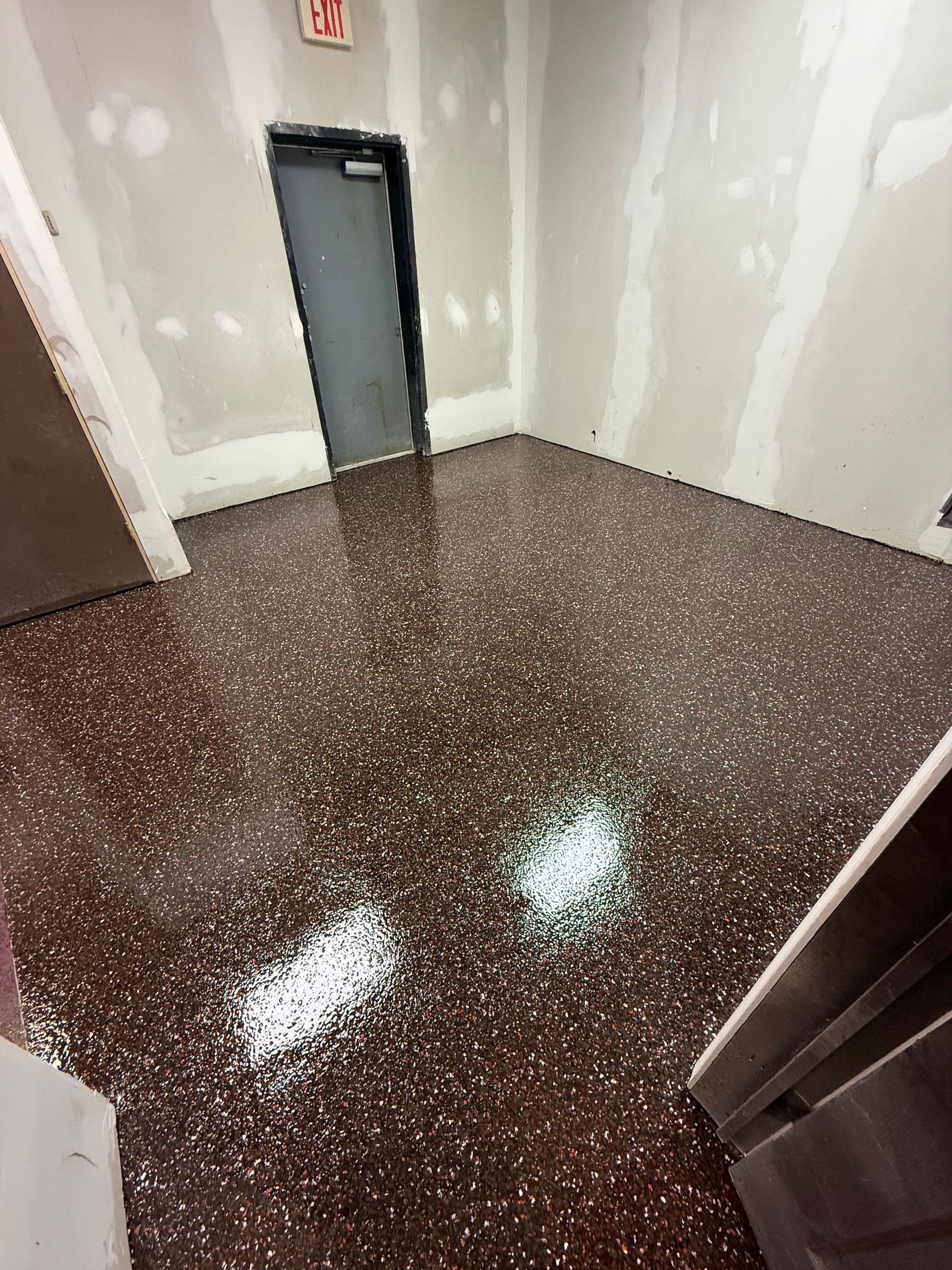 Empty hallway with dark speckled floor and gray doors under bright lights
