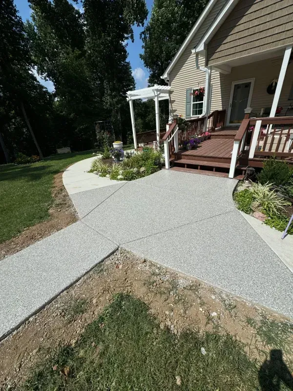 Concrete walkway leading to a house porch, with a ramp and landscaped yard.