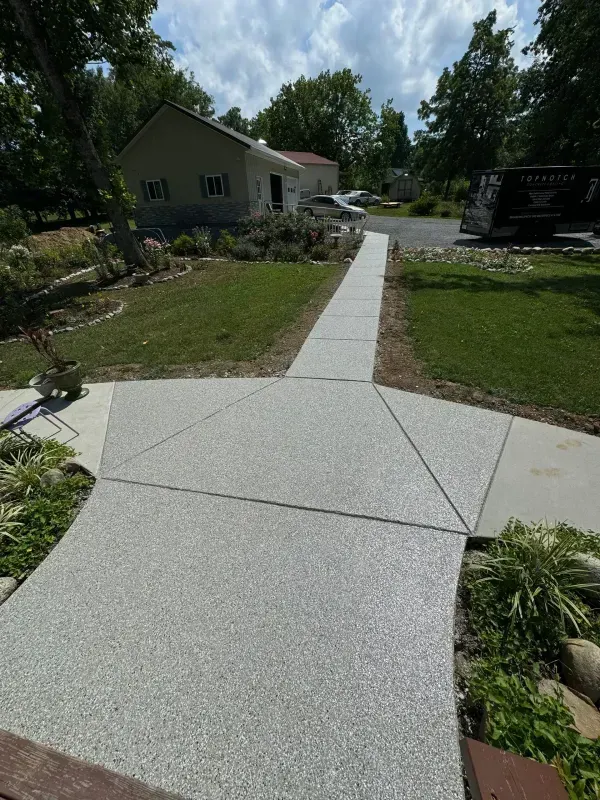 Freshly poured concrete sidewalk leading to a house along a grassy yard on a sunny day