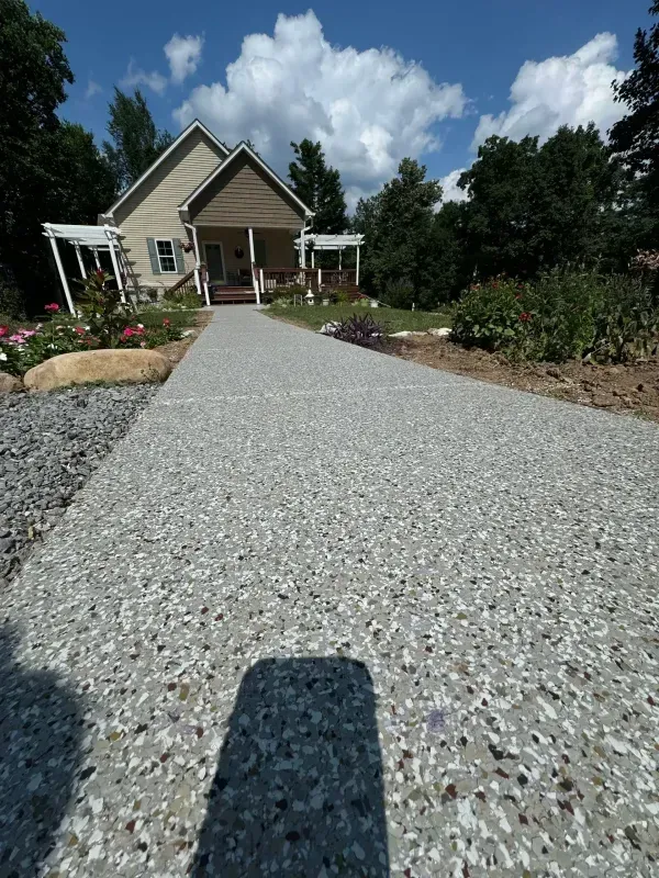 Gravel walkway leading to a house with a porch, landscaped garden, and blue sky with clouds.