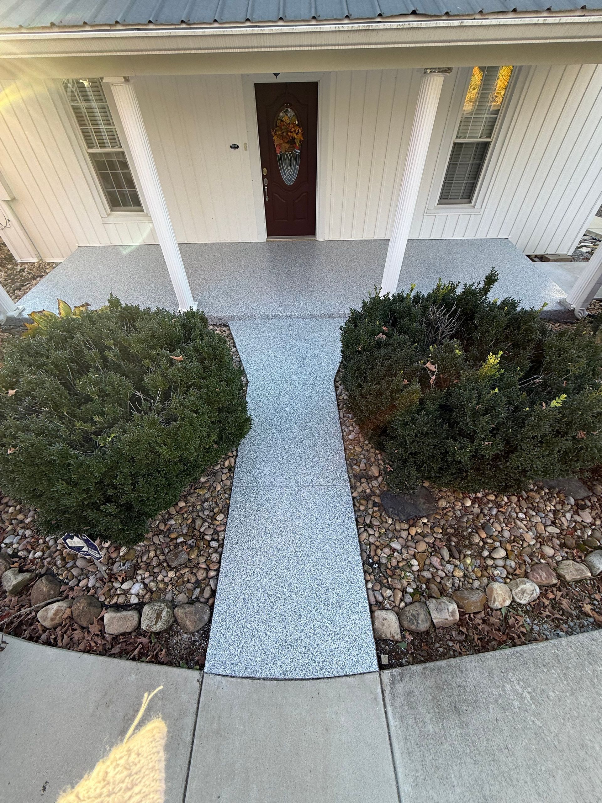 Front porch with a dark door, white columns, gravel path, and trimmed bushes leading to the entrance.