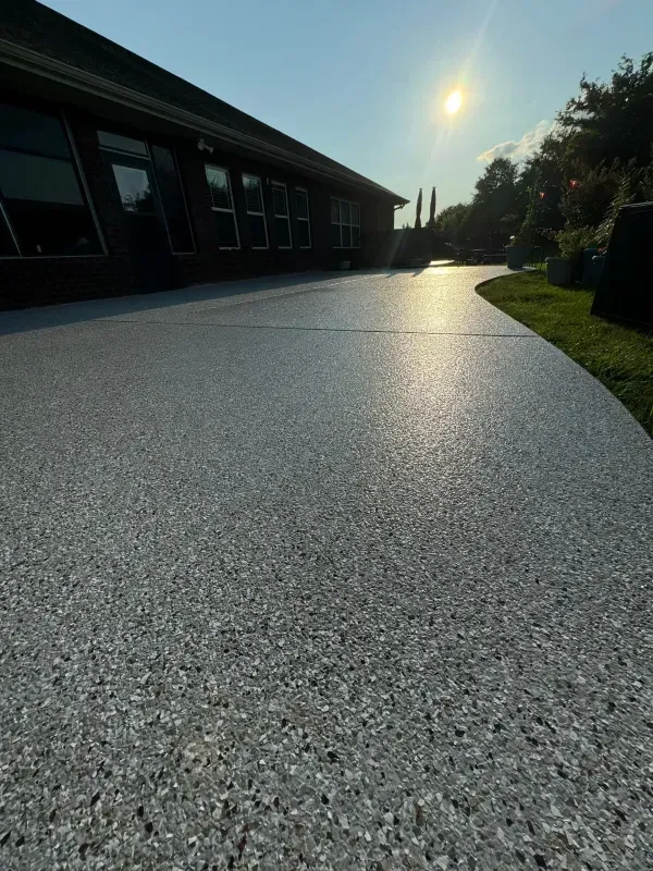 Sunlit gravel path beside a dark building, with grass and trees in the distance.