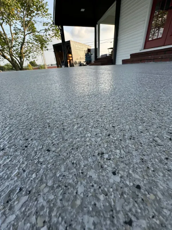 Low-angle view of a speckled concrete porch beside a house, with trees and buildings in the distance.