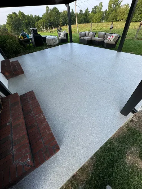 Covered patio with light gray floor, brick steps, and outdoor seating overlooking a grassy yard