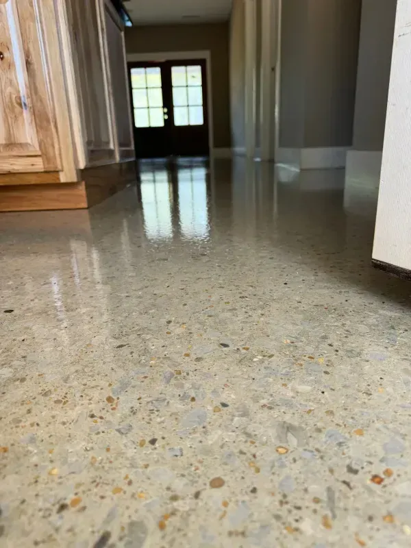 Polished speckled kitchen floor leading to a doorway with sunlight beyond